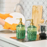 Two green soap dispensers with gold pumps on a kitchen counter.