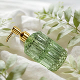 Green glass dispenser with gold pump against a white fabric and green leafy background