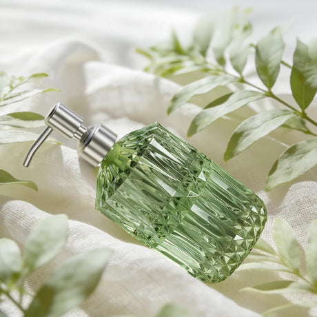 Green diamond-shaped bottle with silver pump on a white fabric background with green leaves