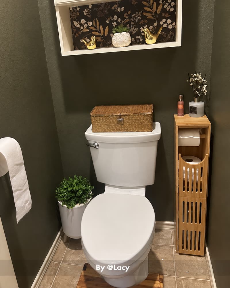 AmazerBath bamboo toilet paper storage cabinet beside a white toilet, topped with bottles and a small plant.