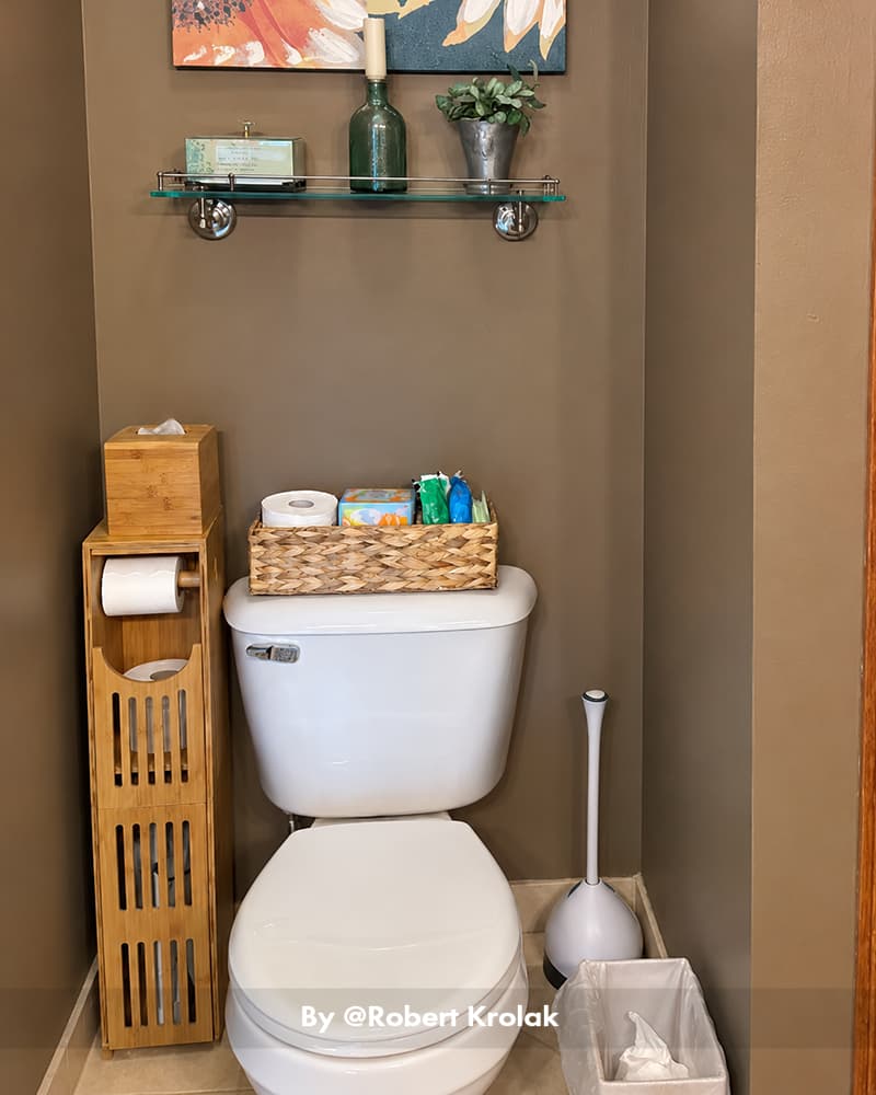 AmazerBath bamboo toilet paper storage cabinet holding rolls beside a white toilet with baskets and wall shelves.