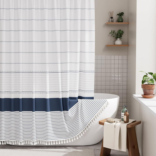 AmazerBath navy blue farmhouse shower curtain with faux linen texture and boho tassels styled beside a bathtub.