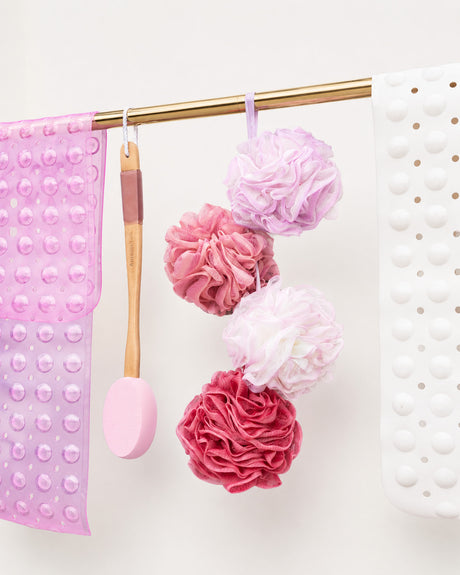 Pink and red bath poufs hanging on a gold rod with pink and white textured towels.
