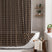 AmazerBath brown grid linen shower curtain: a grid curtain with white tassel trim hangs beside a bathtub in a bright bathroom.
