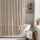 AmazerBath taupe striped linen curtain: textured fabric and white tassel trim frame a bathtub in a bright, neutral bathroom.