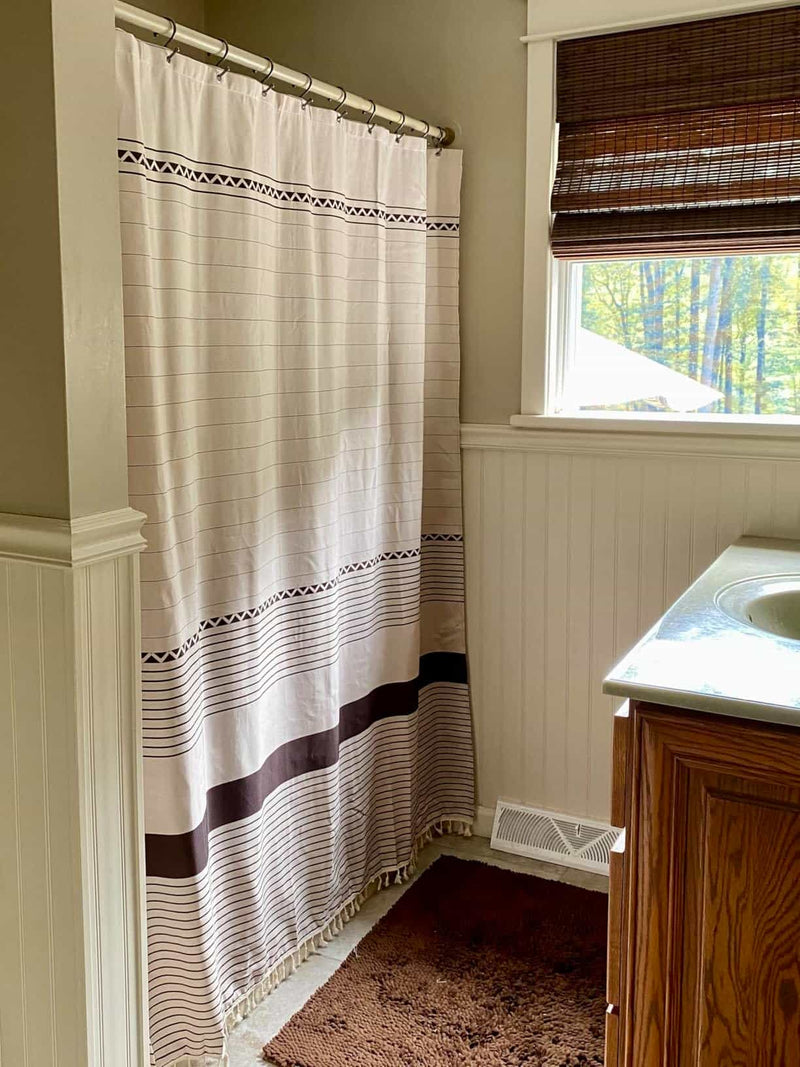 Bathroom with striped shower curtain, wooden vanity, and window with blinds.