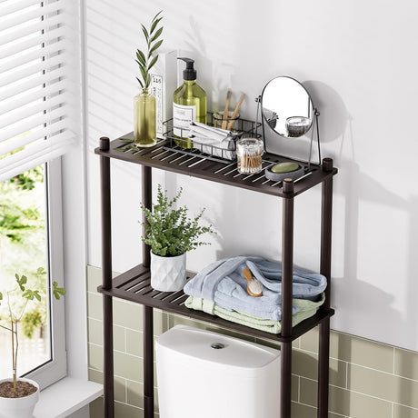 AmazerBath Espresso bamboo two-tier over-the-toilet shelf holding toiletries, folded towels, a mirror, and a plant above a toilet.