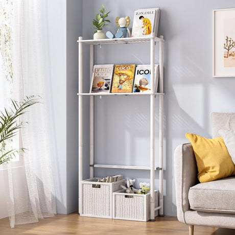 AmazerBath White bamboo two-tier over-the-toilet shelf used beside a sofa for books, decor, and storage baskets.