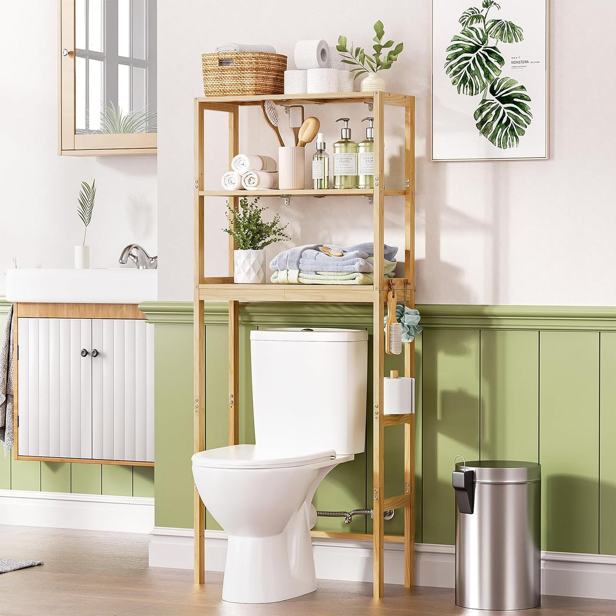 AmazerBath pine three-tier over toilet rack: the rack stands above a toilet with towels, baskets, and plants in a bright bathroom.